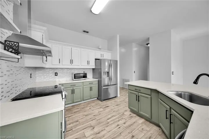 Kitchen featuring green cabinetry, stainless steel appliances, wall chimney range hood, a sink, and light wood-style flooring