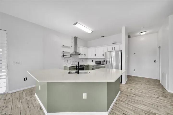 Kitchen with wall chimney exhaust hood, stainless steel appliances, a sink, and light countertops