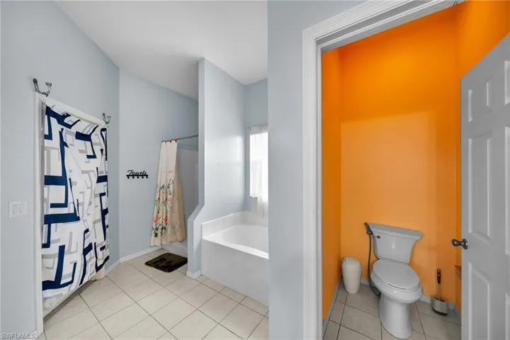 Bathroom with a garden tub, tile patterned floors, toilet, curtained shower, and baseboards