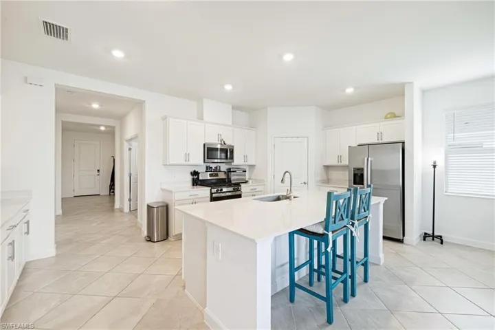 Kitchen with stainless steel appliances, light tile patterned floors, a center island with sink, recessed lighting, and a kitchen bar