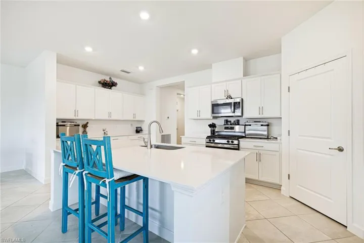 Kitchen featuring appliances with stainless steel finishes, a kitchen breakfast bar, light tile patterned floors, a kitchen island with sink, and white cabinetry