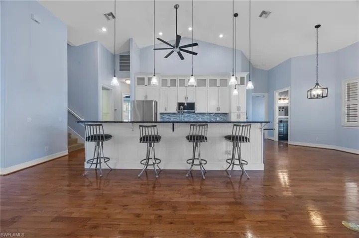 Kitchen featuring glass fronted cabinets, white cabinetry, a kitchen bar, ceiling fan, and dark wood-style floors