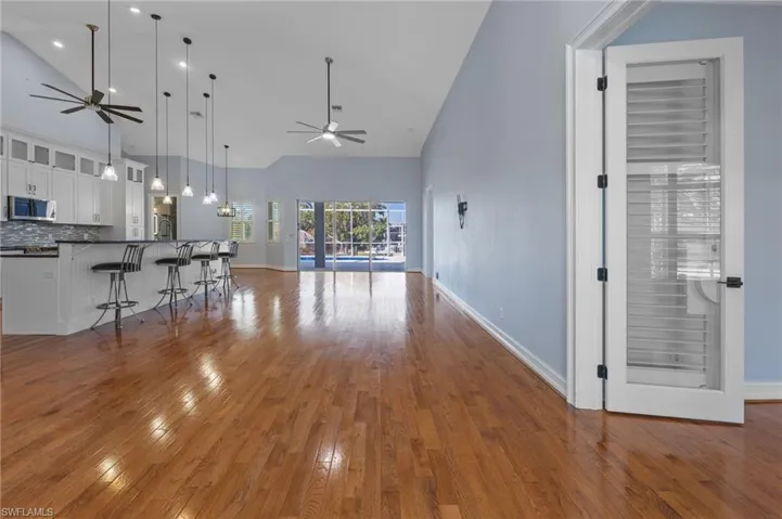 Living area with vaulted ceiling, dark wood finished floors, hanging lights, and a ceiling fan