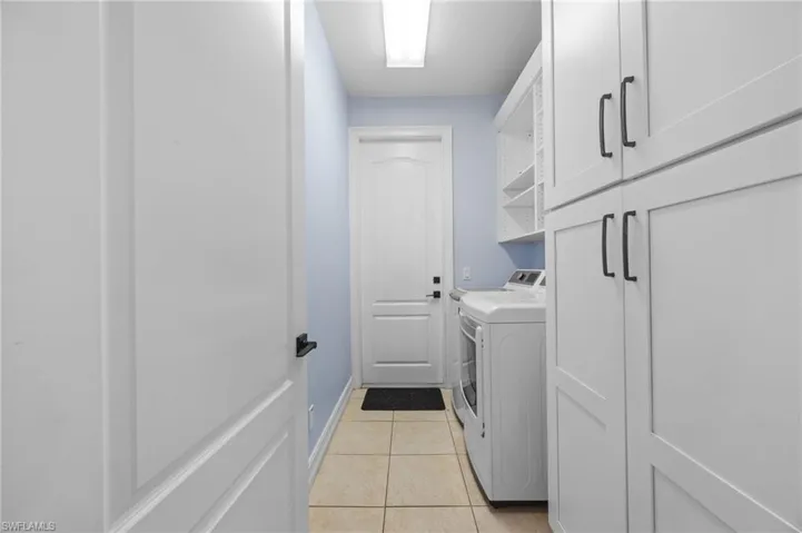 Laundry room featuring separate washer and dryer, light tile patterned flooring, and cabinet space