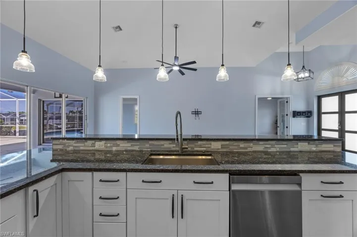 Kitchen with plenty of natural light, pendant lighting, white cabinets, and lofted ceiling