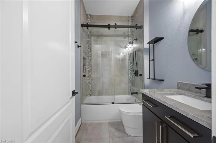 Bathroom with bath / shower combo with glass door, vanity, and a textured wall