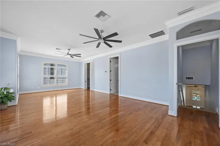 Unfurnished living room featuring ornamental molding, wood-type flooring, and a ceiling fan