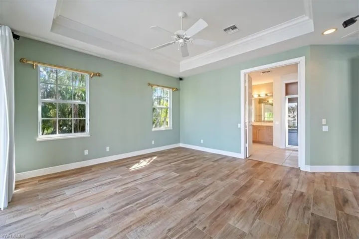 Empty room featuring a healthy amount of sunlight, light wood-type flooring, crown molding, and a tray ceiling