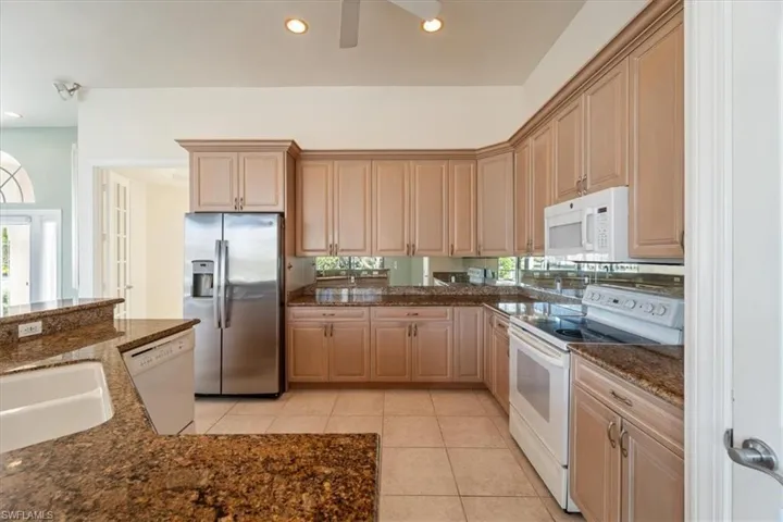 Kitchen featuring light tile patterned floors, light brown cabinetry, sink, dark stone countertops, and white appliances