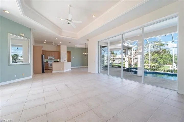Unfurnished living room with ceiling fan with notable chandelier, a healthy amount of sunlight, a raised ceiling, and light tile patterned floors