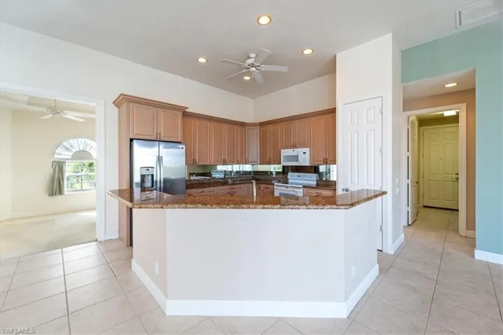 Kitchen with ceiling fan, white appliances, dark stone countertops, and a kitchen island