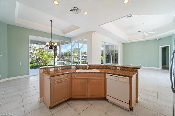Kitchen with white dishwasher, a kitchen island with sink, and a tray ceiling