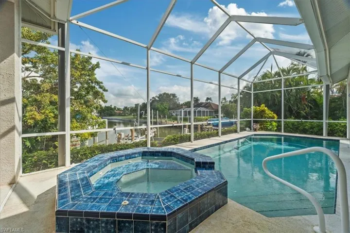 View of swimming pool featuring glass enclosure, a water view, a patio, and an in ground hot tub