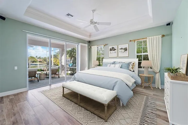 Bedroom with ceiling fan, access to exterior, light hardwood / wood-style floors, and a raised ceiling