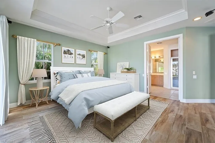 Bedroom with connected bathroom, ceiling fan, crown molding, a tray ceiling, and light hardwood / wood-style flooring