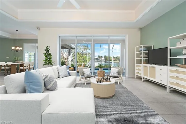 Living room with ceiling fan with notable chandelier, a healthy amount of sunlight, crown molding, and a tray ceiling