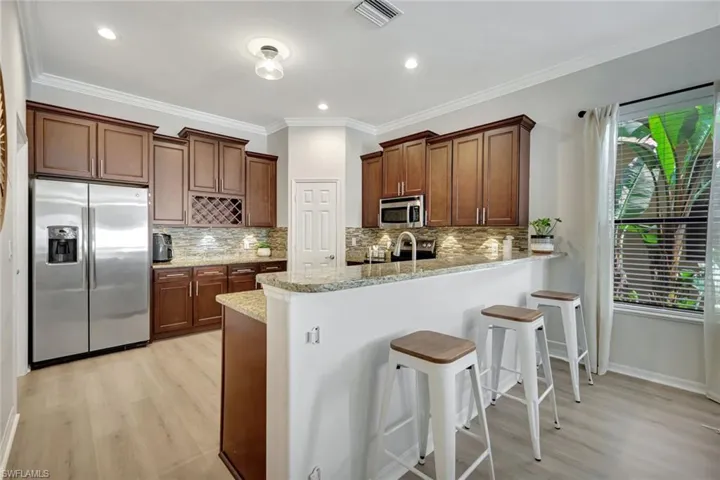 Kitchen featuring stainless steel appliances, light wood finished floors, a breakfast bar area, ornamental molding, and light stone counters