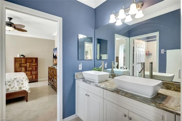 Ensuite bathroom featuring crown molding, double vanity, a chandelier, and tile patterned floors