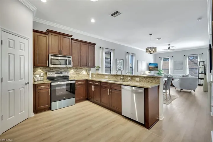 Kitchen with stainless steel appliances, a peninsula, open floor plan, ornamental molding, and tasteful backsplash