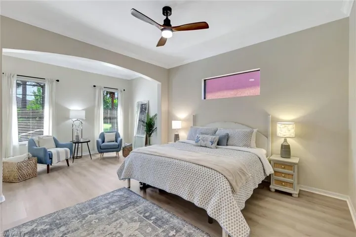 Bedroom featuring wood finished floors, crown molding, arched walkways, and ceiling fan