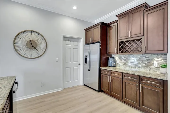 Kitchen with crown molding, stainless steel fridge with ice dispenser, tasteful backsplash, light wood finished floors, and light stone counters