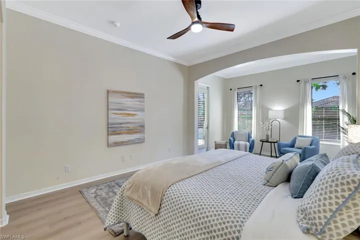 Bedroom with ornamental molding, light wood finished floors, arched walkways, and ceiling fan