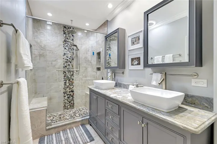 Full bathroom featuring double vanity, tiled shower, crown molding, and recessed lighting