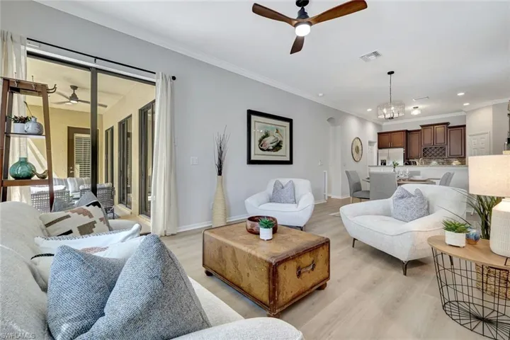 Living room featuring a ceiling fan, crown molding, light wood-style flooring, arched walkways, and a chandelier