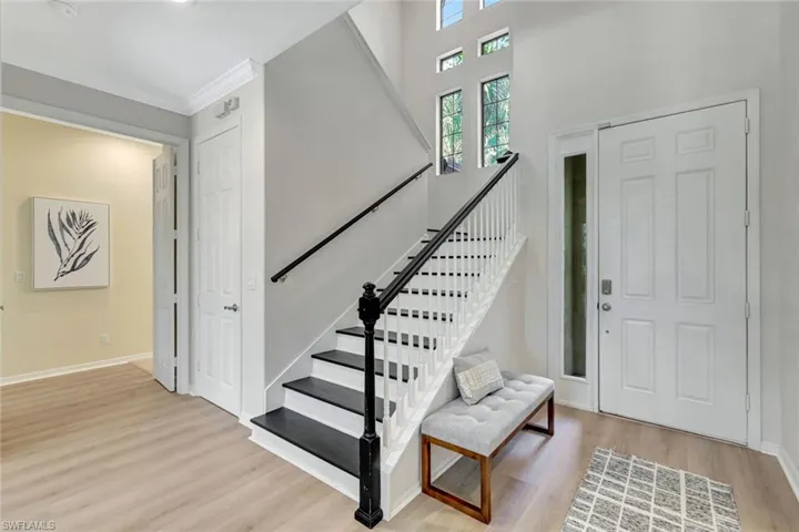 Entryway with light wood finished floors, stairway, crown molding, and a high ceiling