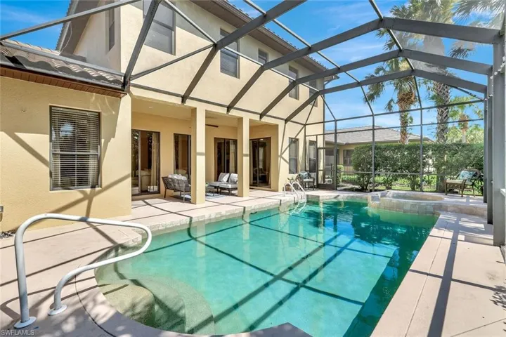 View of swimming pool with a patio area, screened enclosure, and a pool with connected hot tub