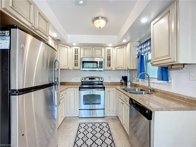 Kitchen featuring light speckled floor, light countertops, appliances with stainless steel finishes, glass insert cabinets, and a sink