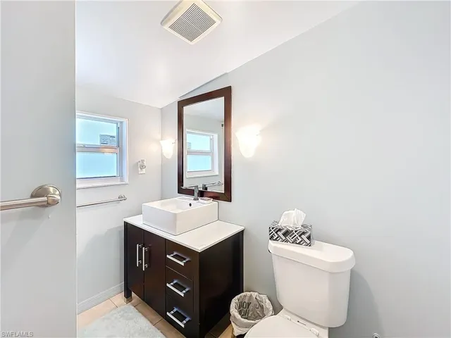 Bathroom with tile patterned flooring, toilet, vanity, visible vents, and vaulted ceiling