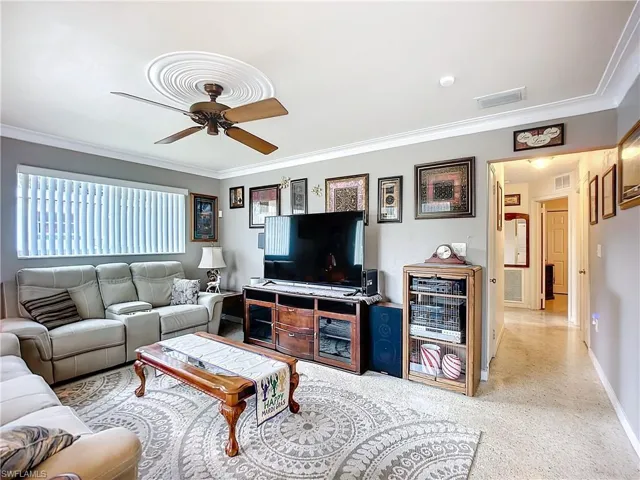 Living area with baseboards, visible vents, ceiling fan, and ornamental molding
