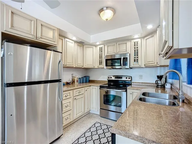 Kitchen featuring light speckled floor, a sink, light countertops, appliances with stainless steel finishes, and glass insert cabinets