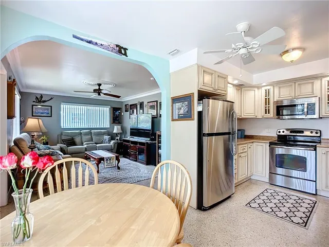 Kitchen with arched walkways, cream cabinets, appliances with stainless steel finishes, glass insert cabinets, and open floor plan