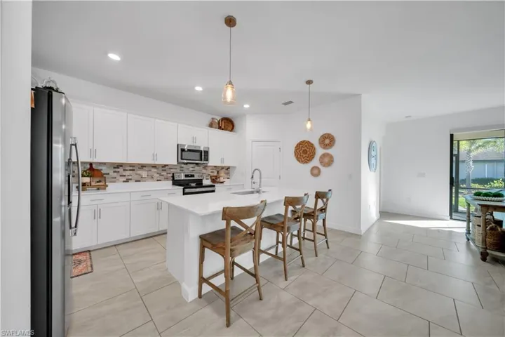 Kitchen featuring appliances with stainless steel finishes, a kitchen breakfast bar, decorative light fixtures, a kitchen island with sink, and white cabinetry