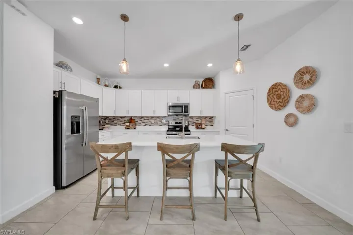 Kitchen featuring appliances with stainless steel finishes, decorative light fixtures, a breakfast bar area, decorative backsplash, and recessed lighting