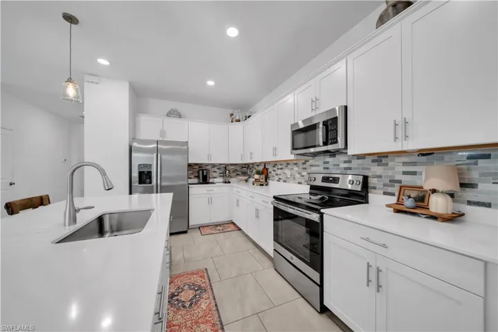 Kitchen featuring appliances with stainless steel finishes, white cabinetry, hanging light fixtures, tasteful backsplash, and recessed lighting