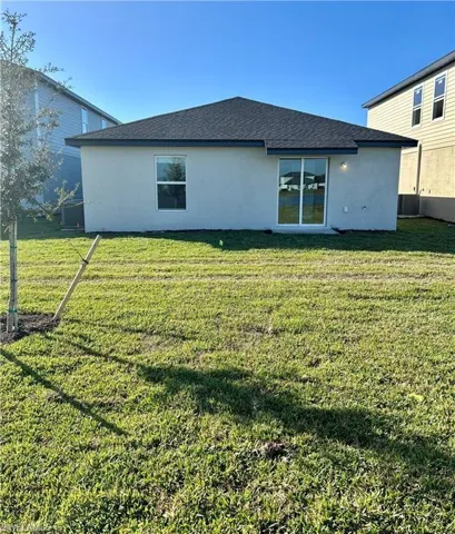 Rear view of property with stucco siding, roof with shingles, and a yard