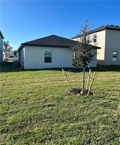 Back of property with stucco siding, a yard, and roof with shingles