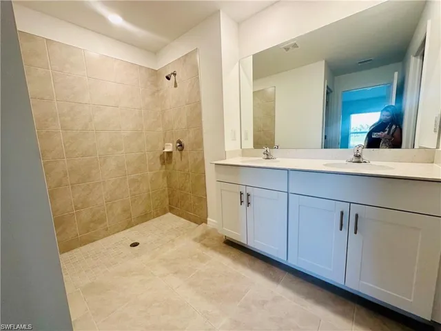 Full bath with double vanity, tiled shower, and light tile patterned floors