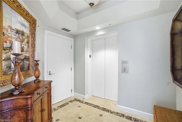 Entryway with inlaid floor details, a raised ceiling, elevator, light tile patterned flooring, and recessed lighting