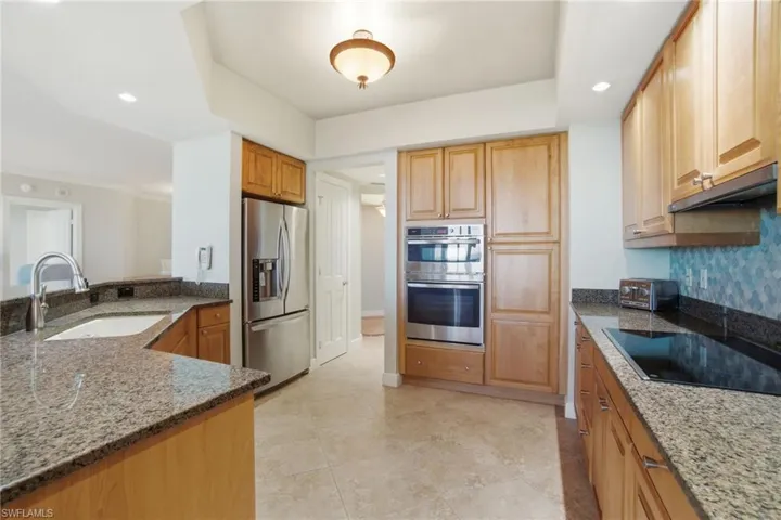 Kitchen featuring dark stone counters, appliances with stainless steel finishes, recessed lighting, under cabinet range hood, and light tile patterned floors