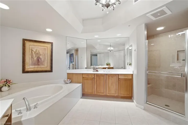 Bathroom featuring vanity, a chandelier, a bath, a stall shower, and light tile patterned flooring