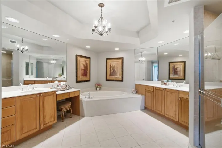 Bathroom with a shower stall, a chandelier, a tray ceiling, a bath, and two vanities