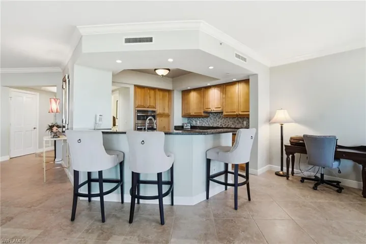 Kitchen featuring backsplash, crown molding, brown cabinetry, a breakfast bar, and recessed lighting