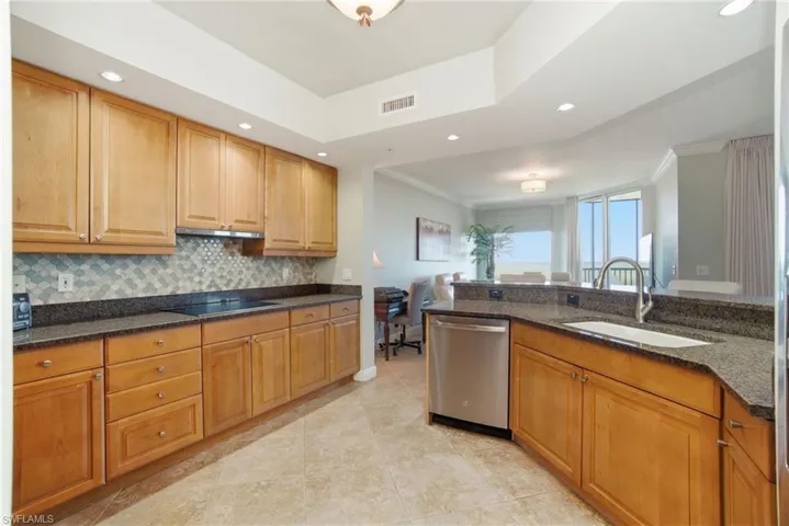 Kitchen featuring stainless steel dishwasher, dark stone countertops, crown molding, brown cabinetry, and recessed lighting