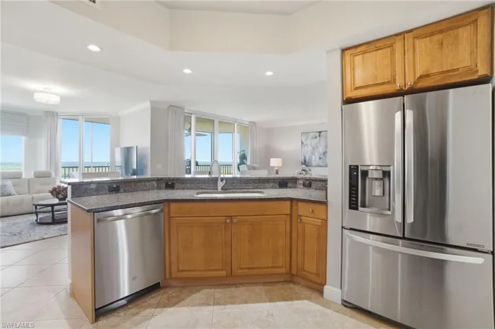 Kitchen featuring stainless steel appliances, open floor plan, brown cabinetry, dark stone countertops, and recessed lighting