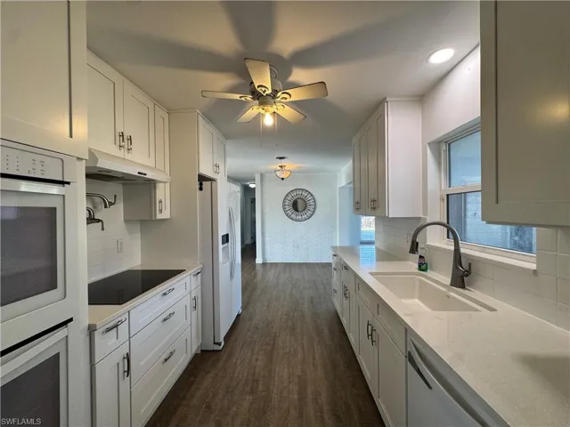 Kitchen with dark wood-style floors, visible vents, a sink, freestanding refrigerator, and white cabinetry