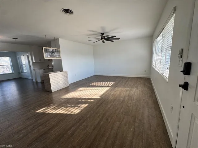 Unfurnished living room with baseboards, visible vents, dark wood-style floors, and ceiling fan